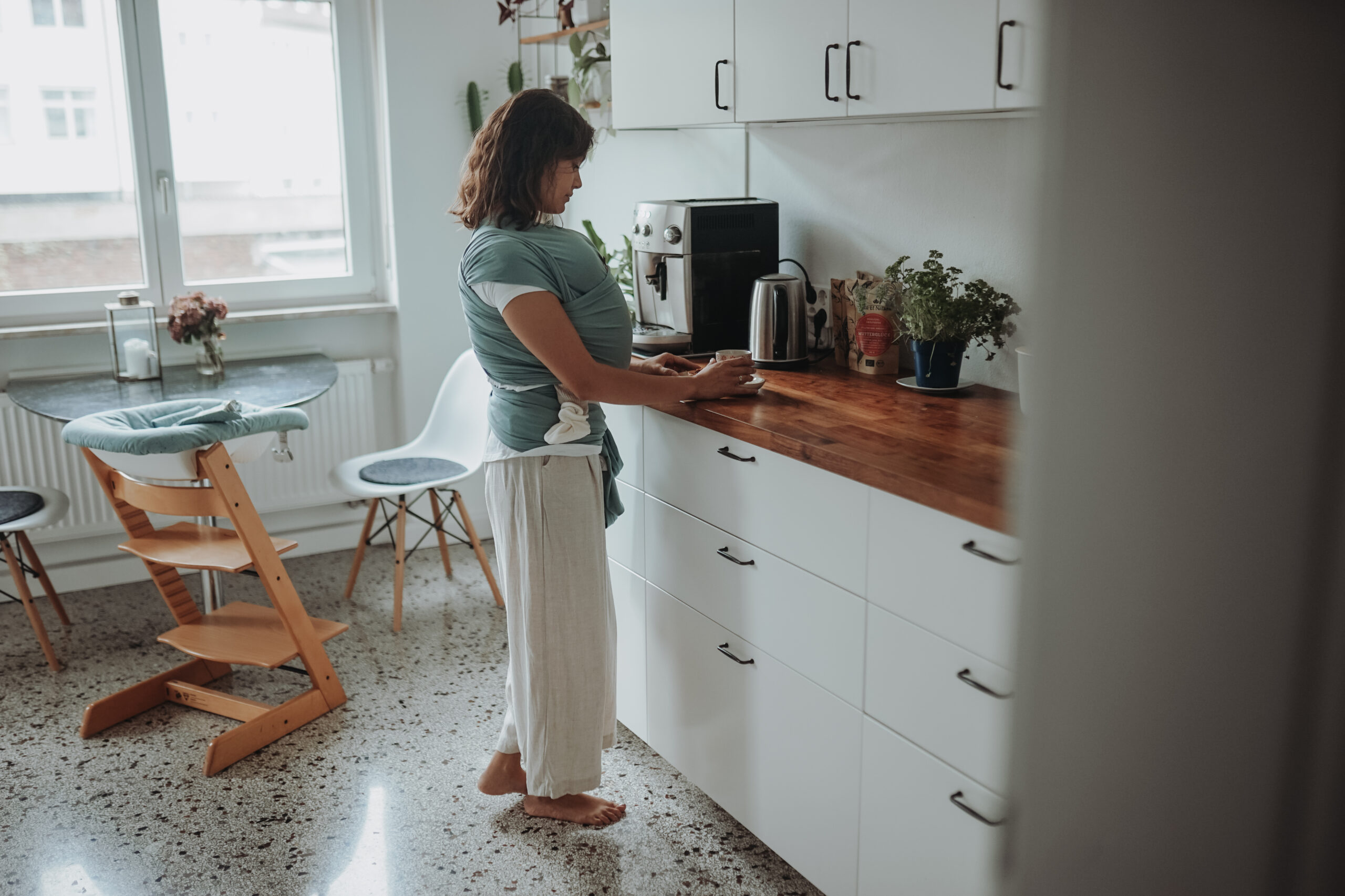 Auf diesem Bild siehst Du eine junge Mama mit ihrem Baby im Tagetuch in ihrem neuen Mama Alltag