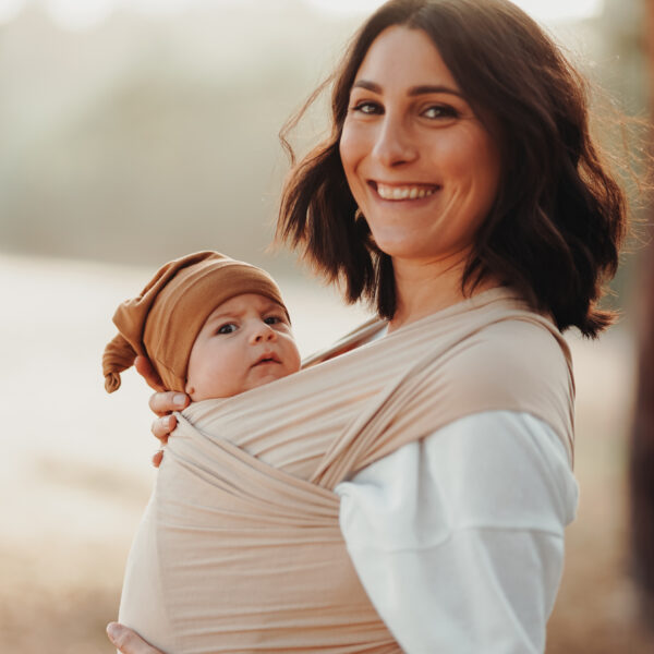 Auf diesem Bild siehst Du eine Mama, die ihr Baby im sandfarbene Babytragetuch trägt