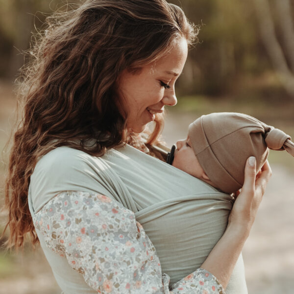 Auf diesem Bild siehst Du eine Frau, die ihr Baby im elastischen Tragetuch in der Farbe Fern trägt