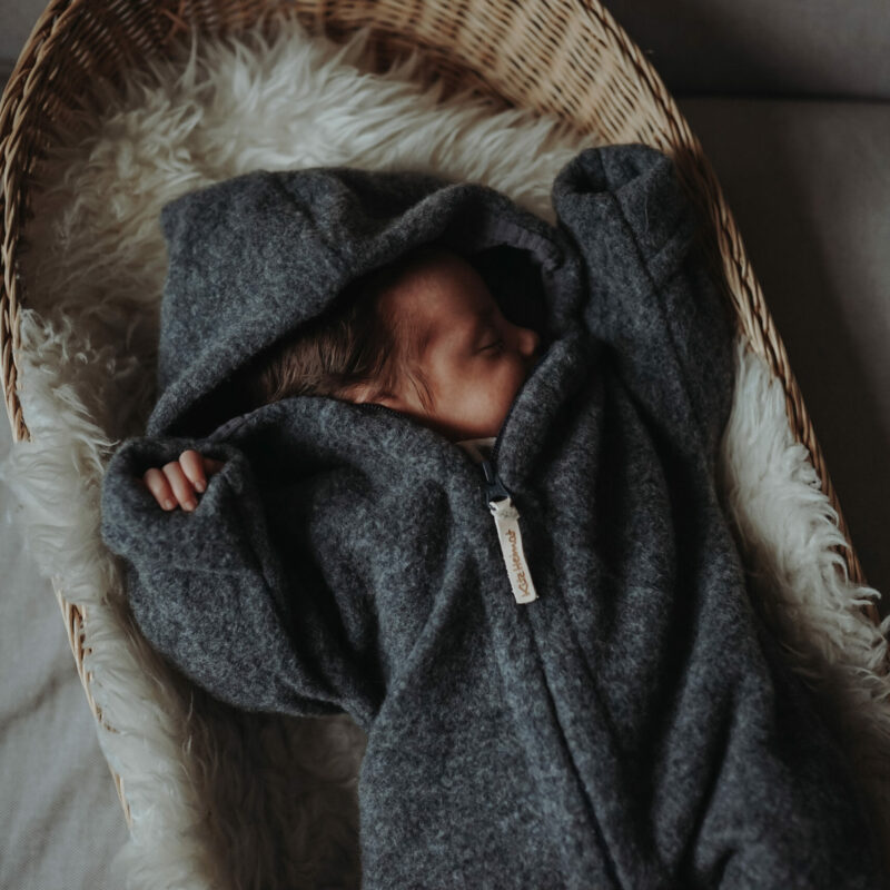 Auf diesem Foto siehst Du ein Neugeborenes, das einen Kitzheimat Overall aus Merinofleece trägt.